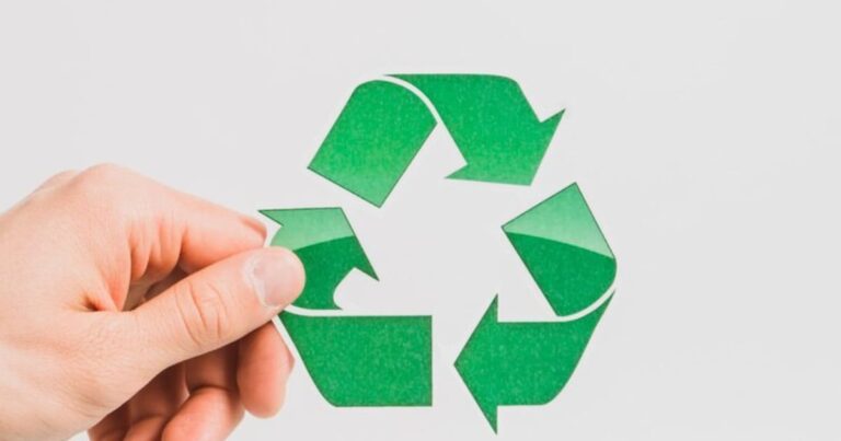 Uma mão segura o símbolo de reciclagem verde, que simboliza a importância da redução de resíduos e práticas de lixo zero.