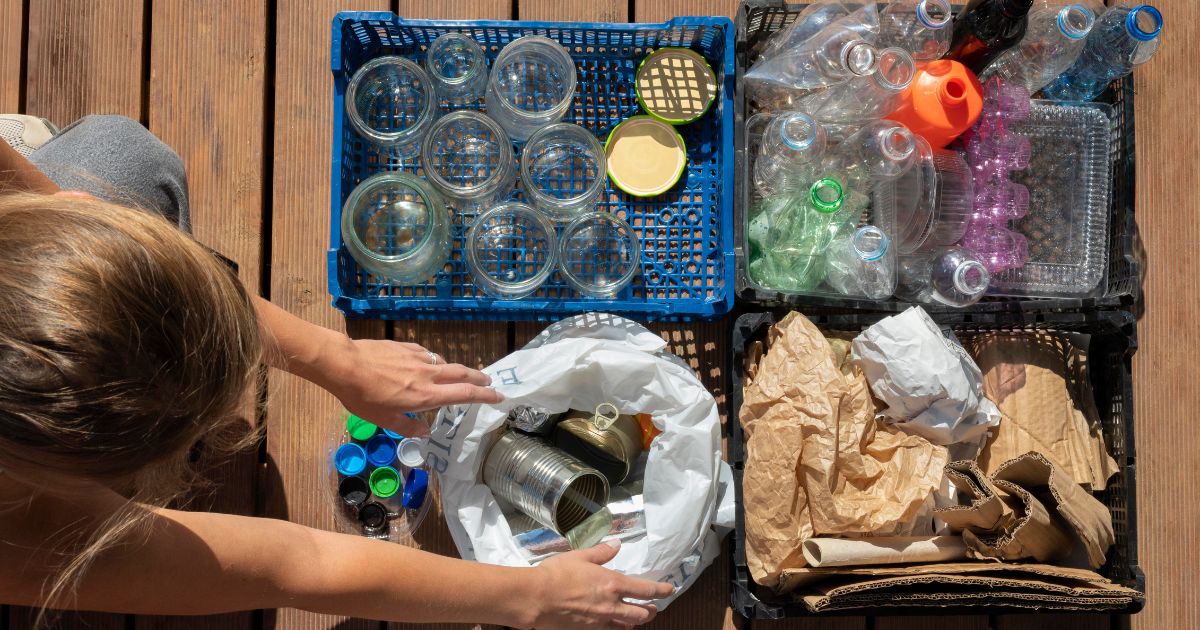 Mulher separa lixo reciclável em caixas para vidro, lata, plástico e papel, destacando o papel da reciclagem para o planeta.