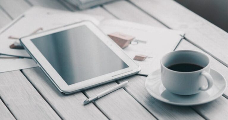 Tablet e xícara de café em mesa de madeira clara, representando a simplicidade e produtividade no estilo de vida minimalista.