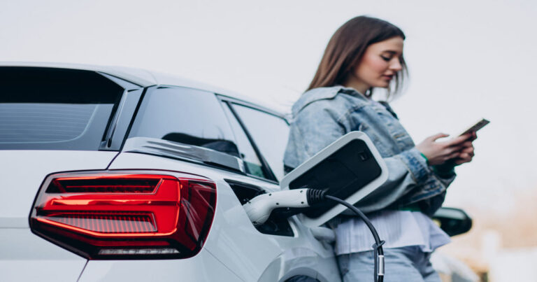 Mulher de jaqueta jeans usa o celular enquanto seu carro elétrico carrega na estação. Combinando modernidade e sustentabilidade.