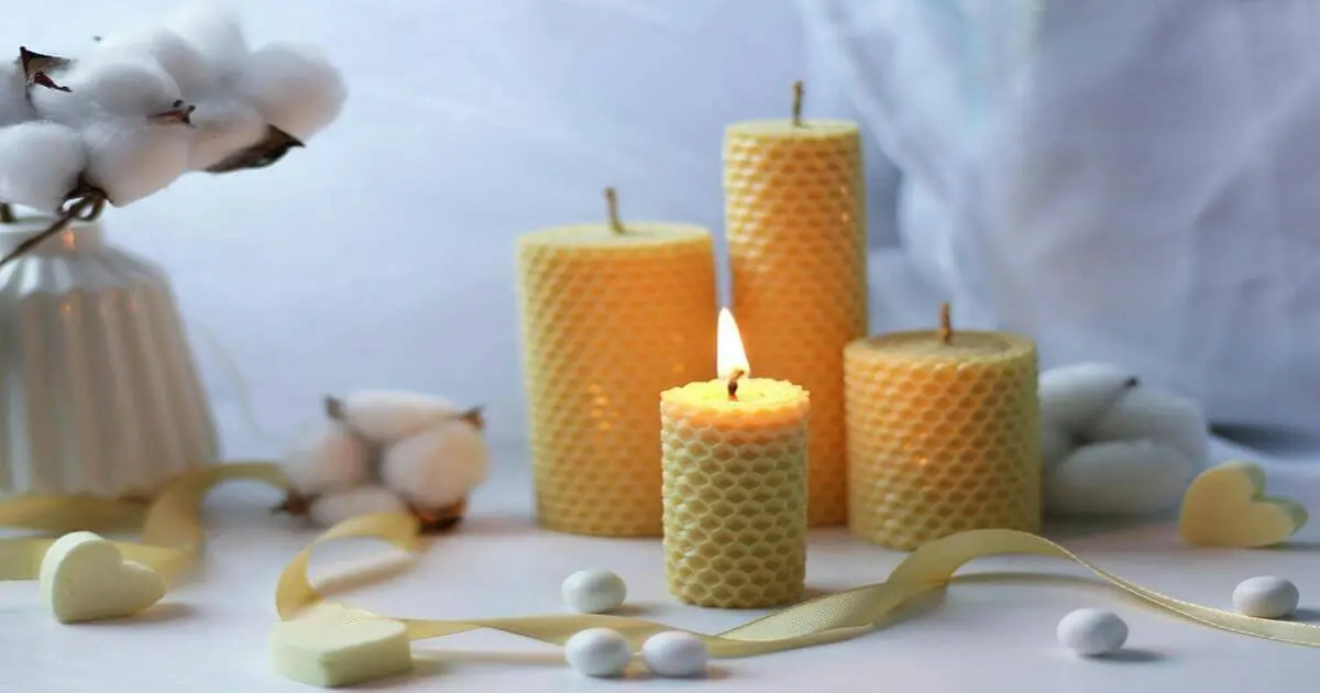 Velas de cera de abelha artesanais, em diferentes tamanhos, decoram uma mesa com algodão e fita amarela.