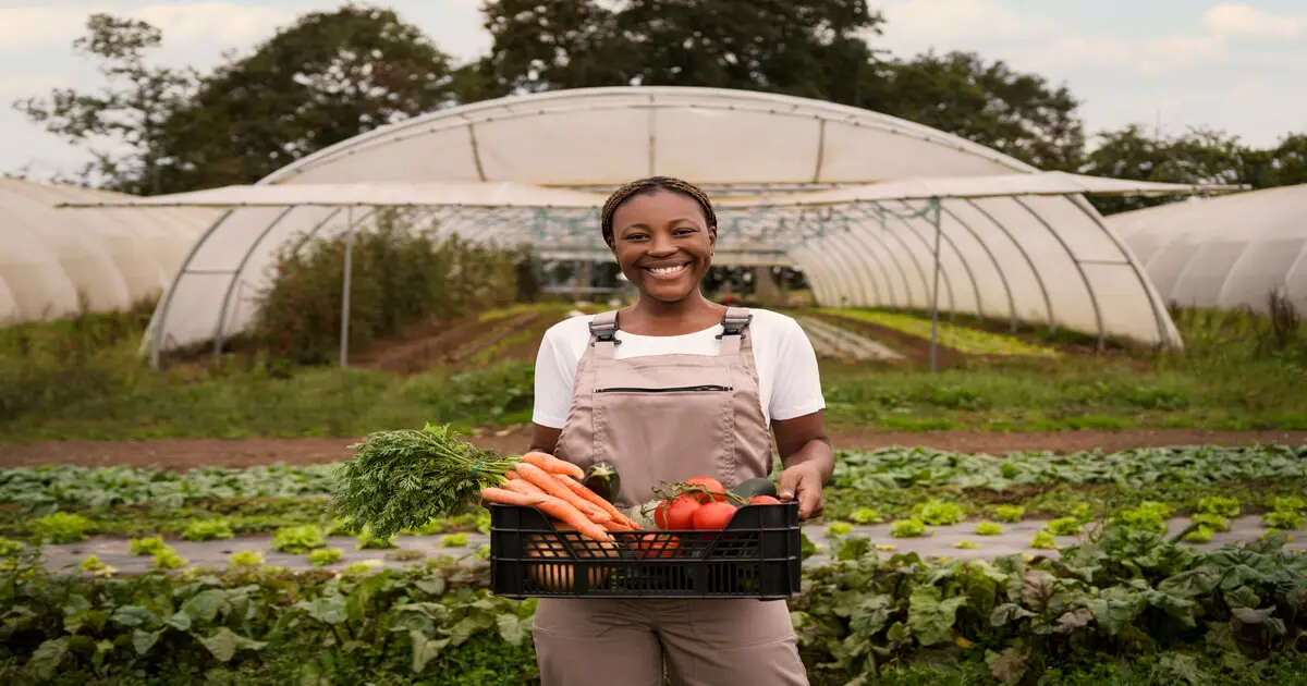 Mulher sorridente em agrofloresta segura cesta com colheita de vegetais frescos, representando agricultura sustentável e biodiversidade.
