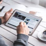 Homem usando um tablet para organizar sua vida digital enquanto toma café, simbolizando produtividade e minimalismo no dia a dia.