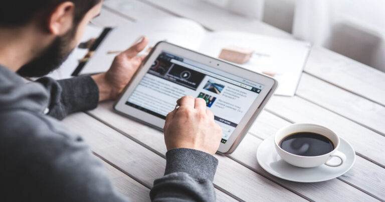 Homem usando um tablet para organizar sua vida digital enquanto toma café, simbolizando produtividade e minimalismo no dia a dia.