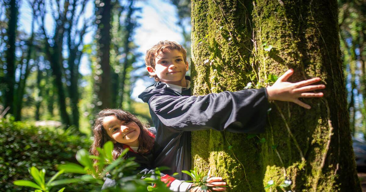 Duas crianças felizes praticam Shinrin-Yoku, o banho de floresta, abraçando uma árvore e desfrutando dos benefícios da natureza para o bem-estar físico e mental.