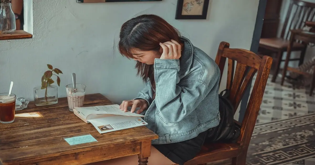 Mulher lendo em uma cafeteria aconchegante, representando um estilo de vida minimalista e organizado, sem distrações digitais.