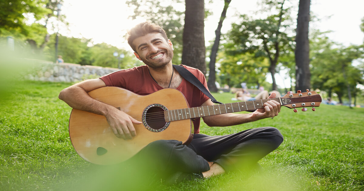 Homem sorridente tocando violão ao ar livre, representando Ikigai, equilíbrio, felicidade e propósito de vida.