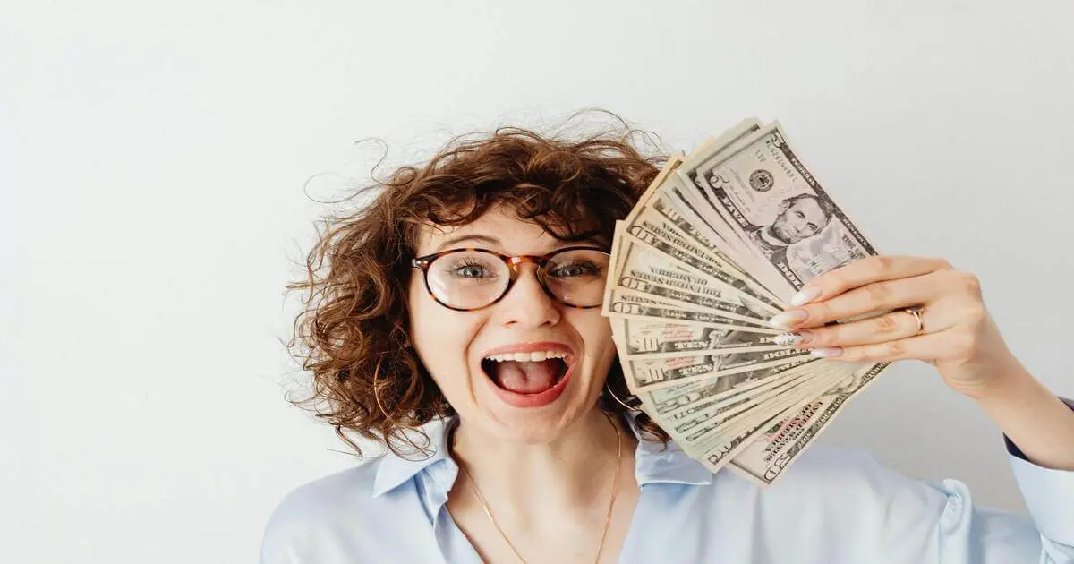 Mulher sorridente segura notas de dólar, representando alegria ao alcançar a liberdade financeira com escolhas conscientes.