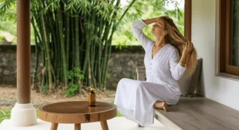 Mulher relaxa ao ar livre aplicando óleo de coco nos cabelos longos, exemplo natural do método no poo como fazer.